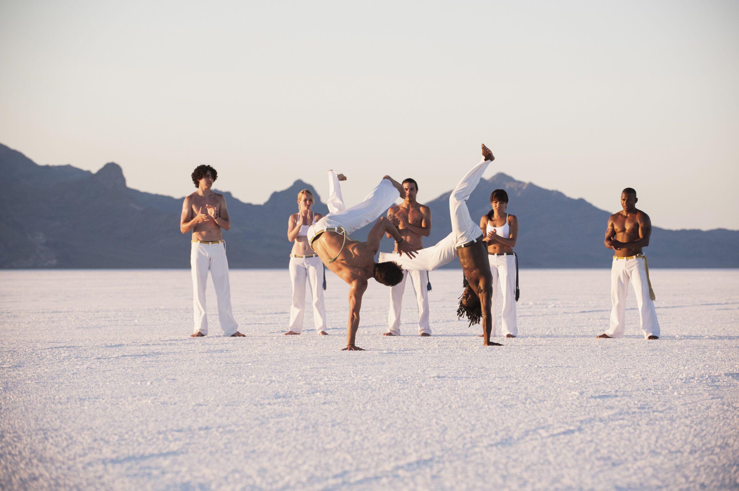 Combate de Capoeira en la Playa: Ritmo y Técnica en Movimiento Dos capoeiristas entrenando en la playa en un combate fluido al ritmo de la música.