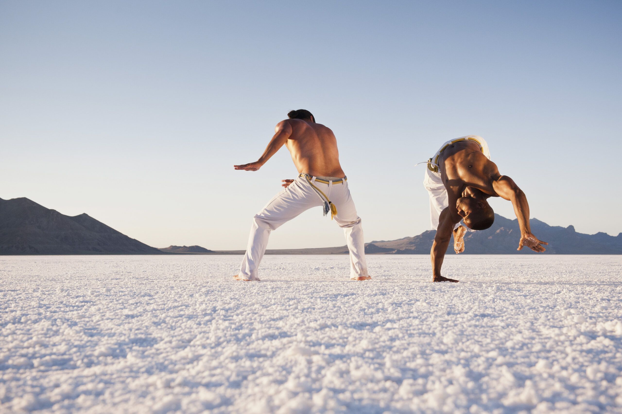 Piruetas en Capoeira: Acrobacia y Arte en Movimiento Capoeirista realizando una pirueta acrobática durante un combate en la playa.
