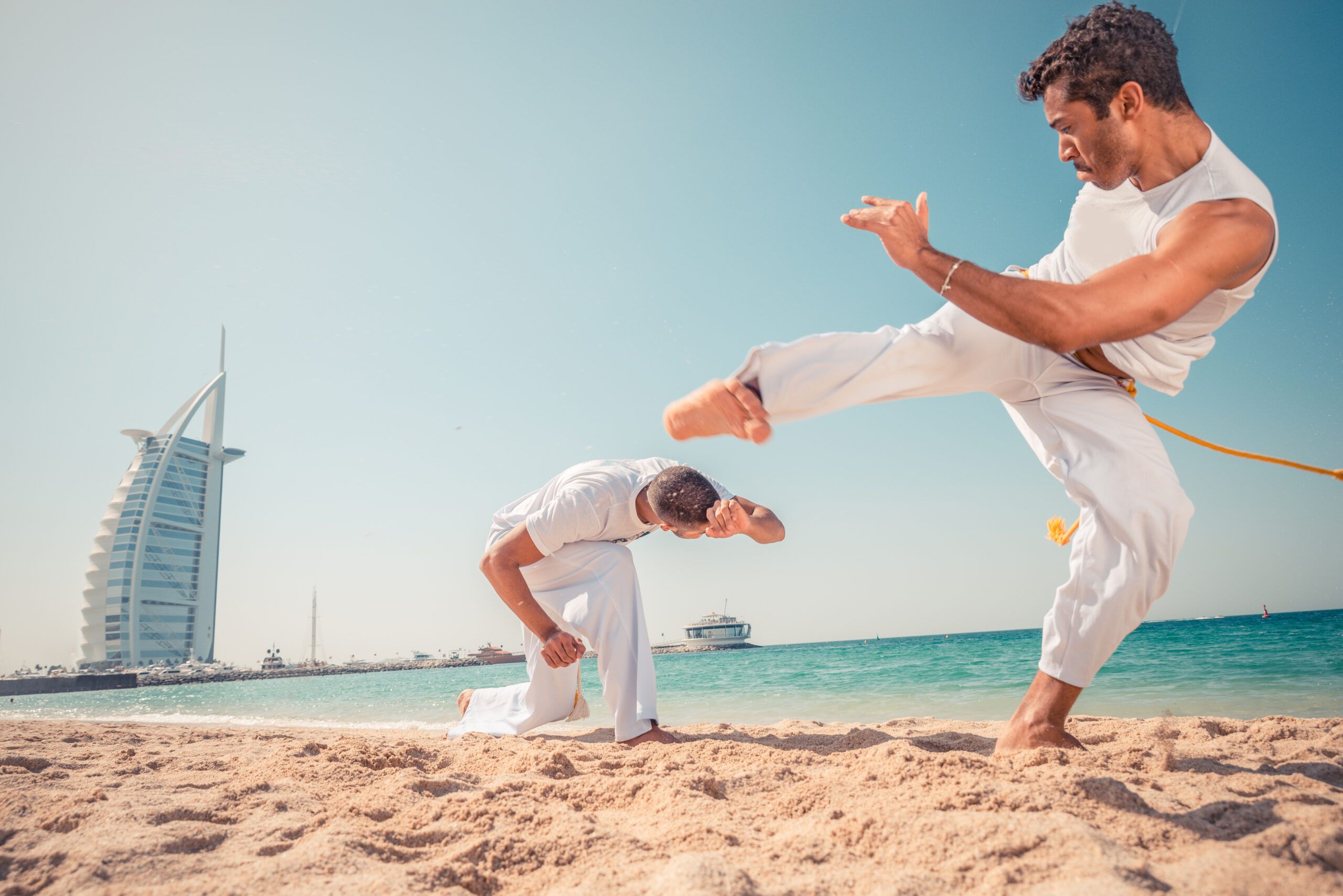 Expresión y Fuerza: Patadas de Capoeira en la Playa Capoeirista ejecutando una patada durante un combate en la playa al ritmo de la música.