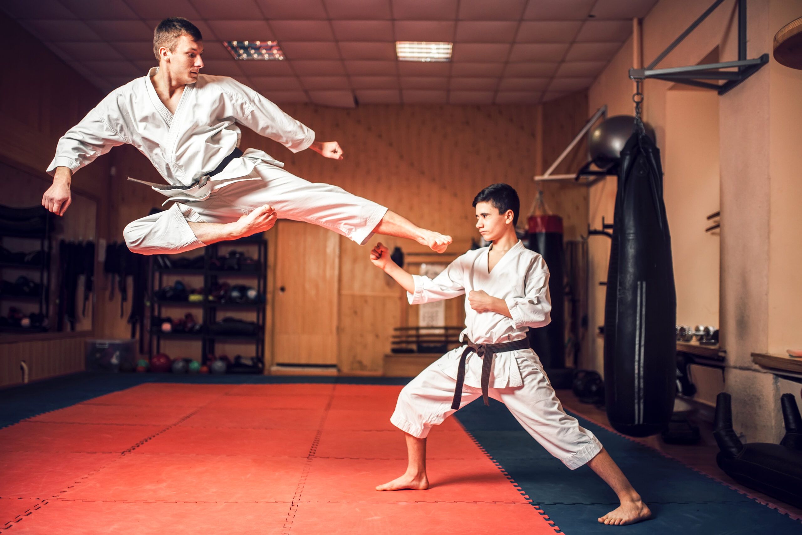 Dos practicantes de karate, uno lanzando una patada y el otro defendiéndose con precisión durante un entrenamiento.